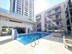 A rooftop swimming pool with a glass balustrade, surrounded by a modern building with balconies. - Amazing Location 2 Br + Maids l 6 sleeps Family (Dubai)