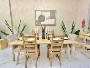 Ein Essbereich mit einem Holztisch, gedeckt für vier Personen, umgeben von Stühlen, einer Vase mit Blumen und einem Feuerlöscher an der Wand.