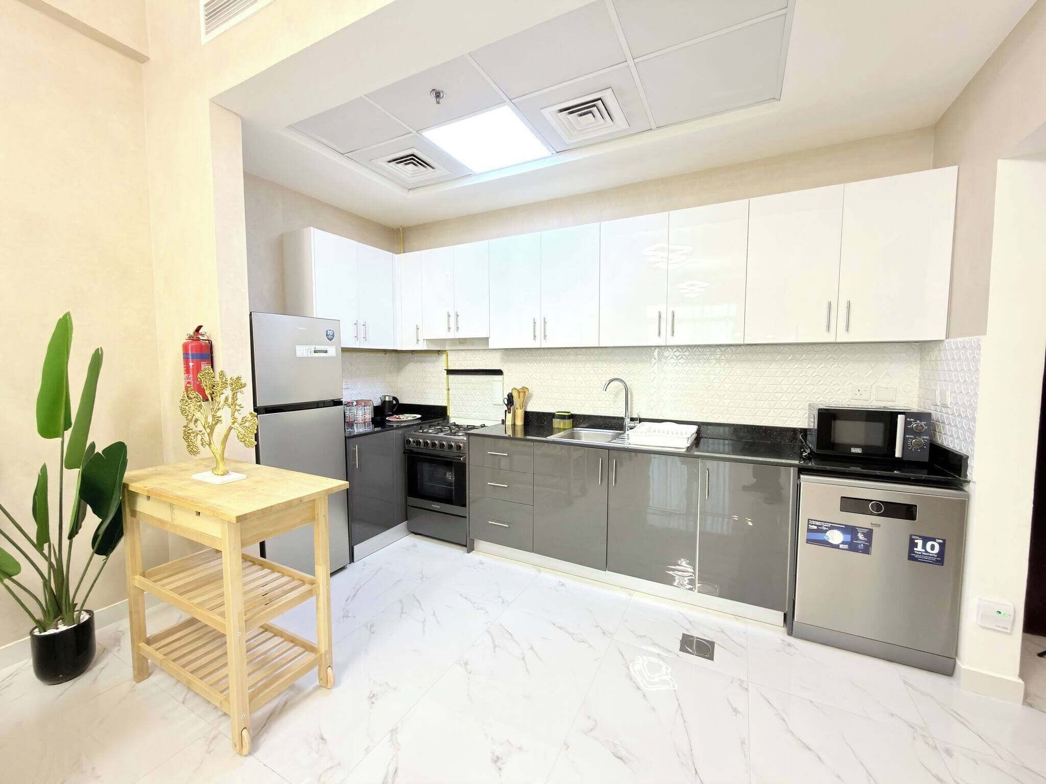 A modern kitchen with white cabinets, a stainless steel refrigerator, a stove, and a microwave.