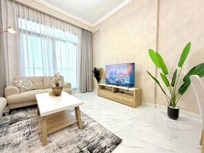 A modern living room with a sofa, coffee table, TV, and a potted plant. - Amazing Location 2 Br + Maids l 6 sleeps Family (Dubai)
