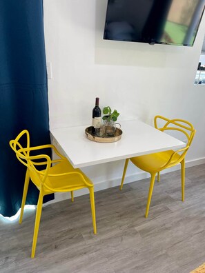 Een kamer met een witte tafel, twee gele stoelen, een fles wijn en een kleine plant op de tafel.
