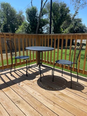 Een houten terras met een ronde tafel en twee stoelen.