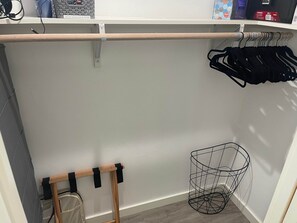 Un armario con barra de madera, una cesta de metal y ropa colgada.