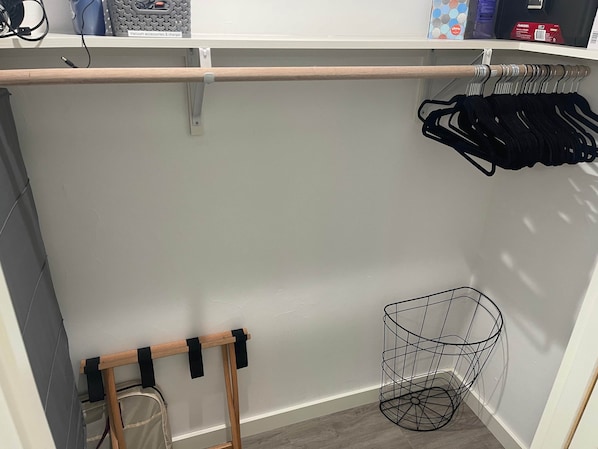 Un armario con barra de madera, una cesta de metal y ropa colgada.