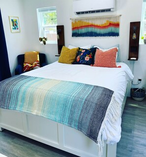 Een bed met een bedovertrek met patroon, een luchtverkoeler aan de muur en een kleurrijke wandtapijt.