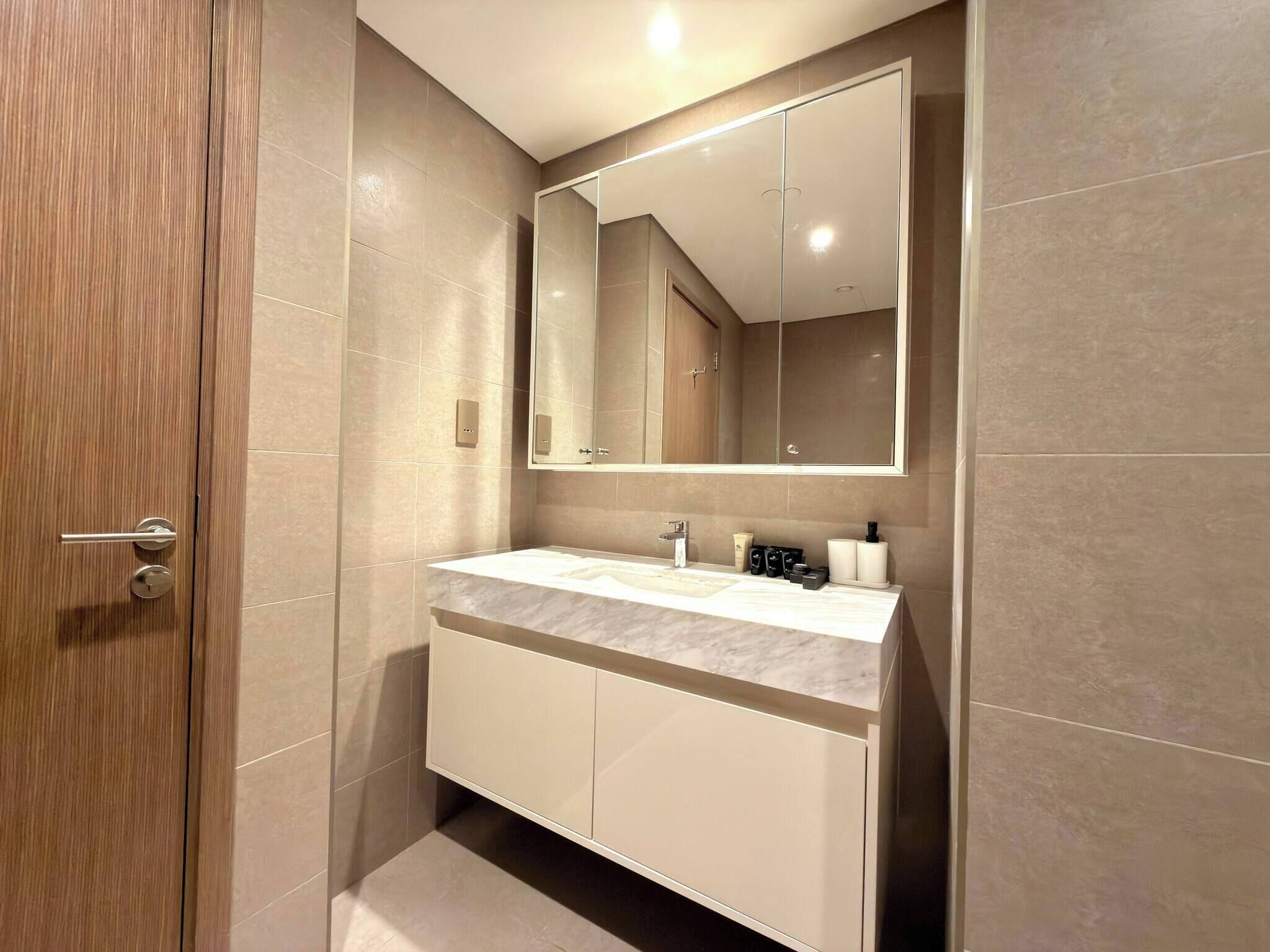 A modern bathroom with a marble sink, a large mirror, and a wooden door.