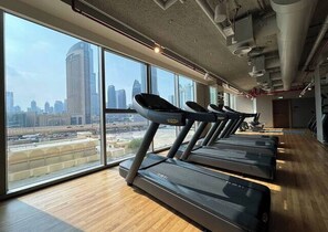 Une salle de sport équipée de tapis de course, dotée de grandes fenêtres et offrant une vue sur la ville.