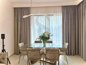 A modern dining room with a glass table surrounded by six chairs, a tripod, and a floral arrangement. - Burj Khalifa View Opposite to Dubai Mall Luxury 2B (Dubai)