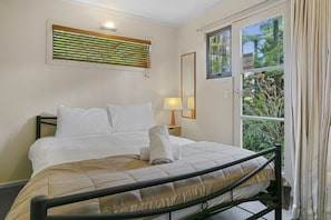A hotel room with a bed, a bedside lamp, a window with a view of greenery, and a door. - Stunning Four Bedroom home near the lake (Taupō)