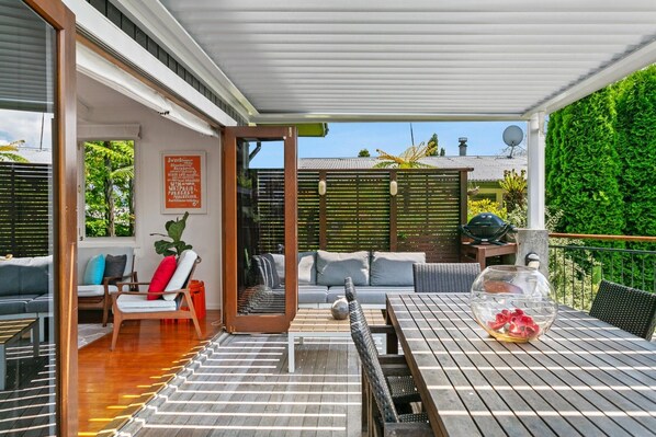Eine überdachte Terrasse im Freien mit einem Holztisch, Stühlen und einer Couch.