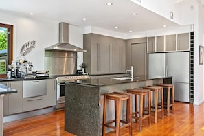 A modern kitchen with stainless steel appliances, a central island with stools, and a large window. - Stunning Four Bedroom home near the lake (Taupō)