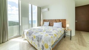 A hotel room with a large bed, a bedside table, a nightstand, a window with curtains, and a view of the outdoors.