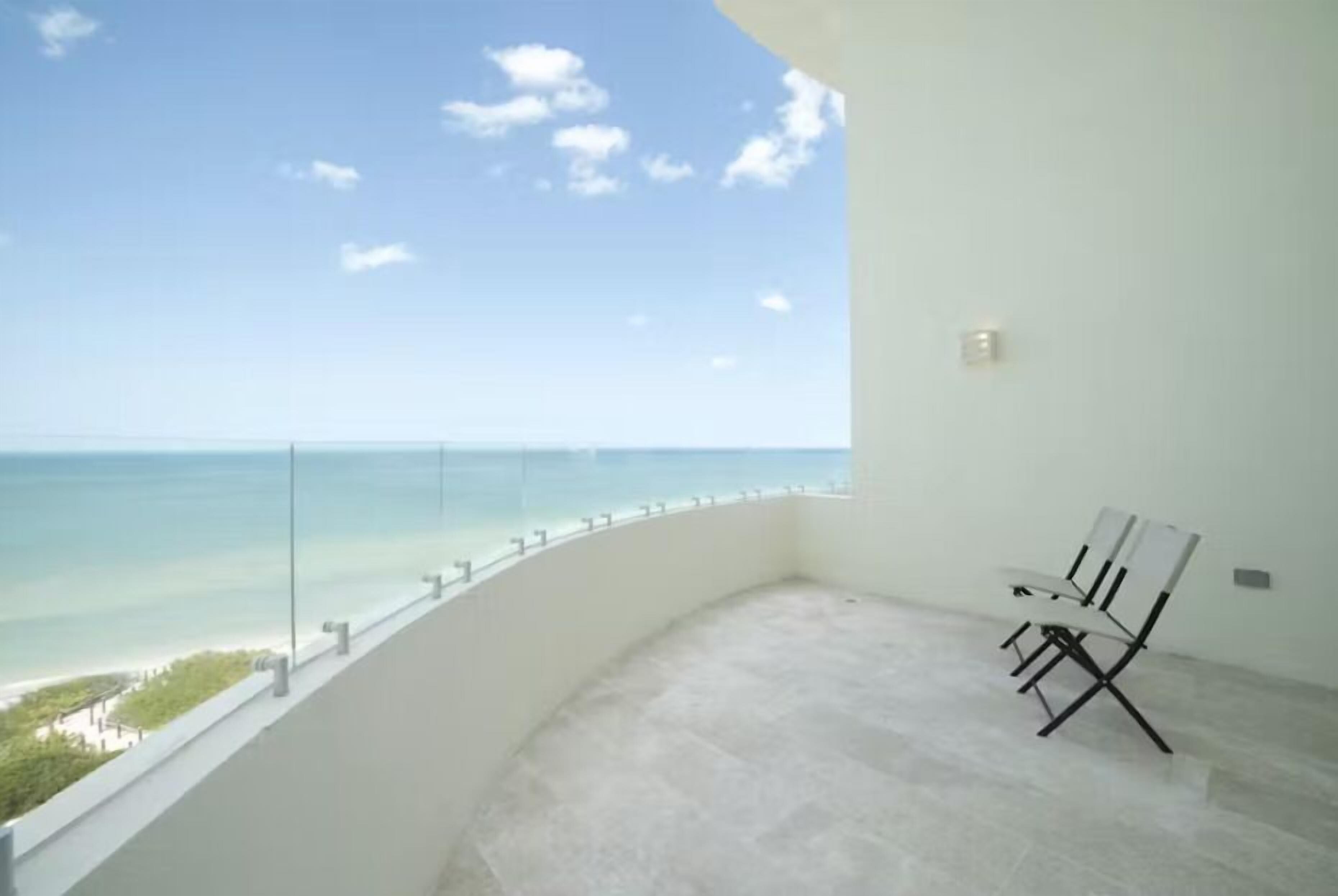 Un balcon offrant une vue dégagée sur l’océan, un mur blanc et une seule chaise.