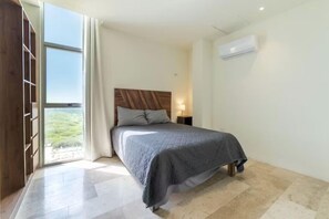 A bedroom with a bed, a nightstand, a window with curtains, and an air conditioning unit.