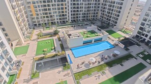 A high-rise residential building with a rooftop pool, green spaces, and a sports court. - Liva 1 BR - Elevated Living at Nshama Tower (Dubai)