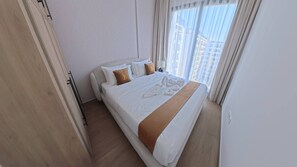 Quarto de hotel com cama, almofadas, roupão e janela com cortinas.