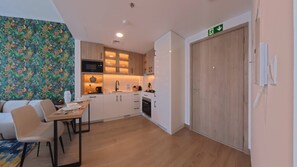 A compact kitchen with white cabinets, a microwave, and a sink. There is a dining area with a table and chairs. - Liva 1 BR - Elevated Living at Nshama Tower (Dubai)