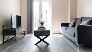Uma sala de estar moderna com televisão de tela plana em um suporte preto, sofá cinza e mesa de centro com livros.