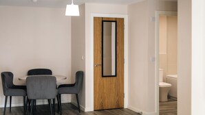 Uma sala de jantar com uma mesa redonda e quatro cadeiras, uma porta de madeira com um espelho e um aparelho de iluminação acima.