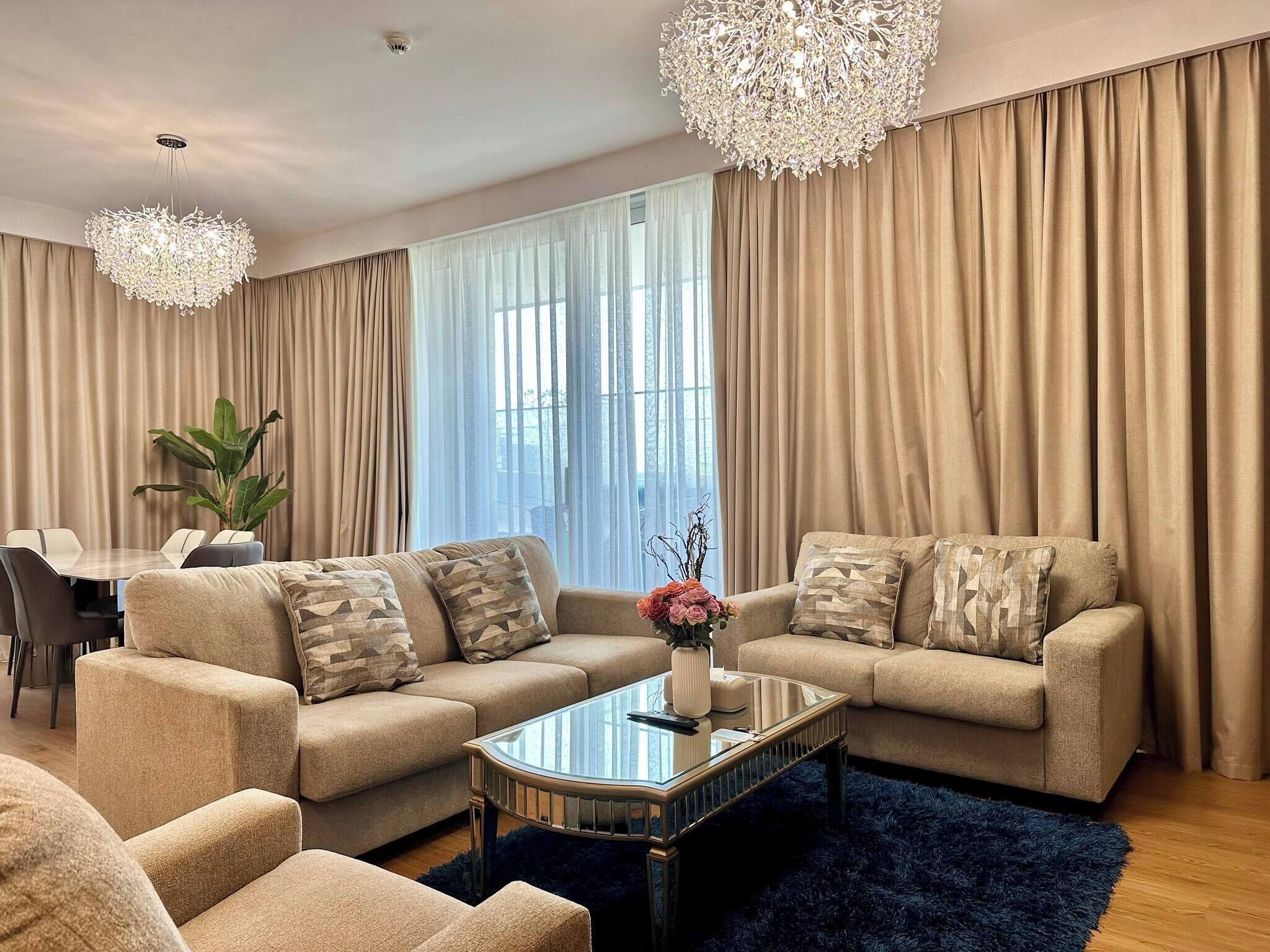 Un salon moderne avec un ensemble de canapés beige, une table basse en verre et un grand lustre.