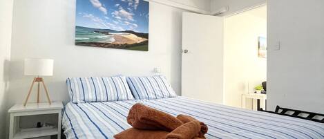 A bedroom with a bed, a nightstand, a lamp, and a painting of a beach scene.