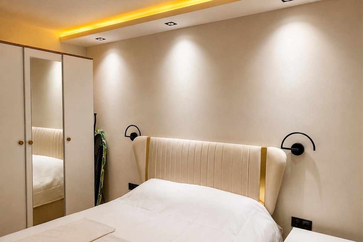 Quarto com cama, mesa de cabeceira, espelho e luminária na parede.