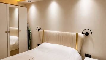 A bedroom with a bed, a nightstand, a bedside table, a mirror, and a wall-mounted light fixture.