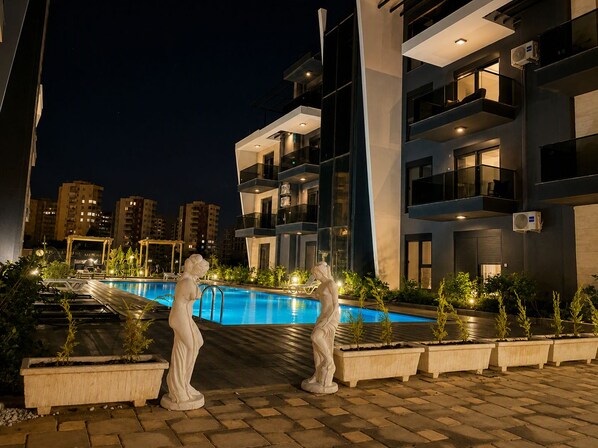 A modern building with a pool, outdoor lighting, and a statue.
