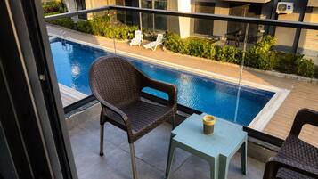Un balcón con piscina, una silla, una mesa y vista a un edificio con balcones.