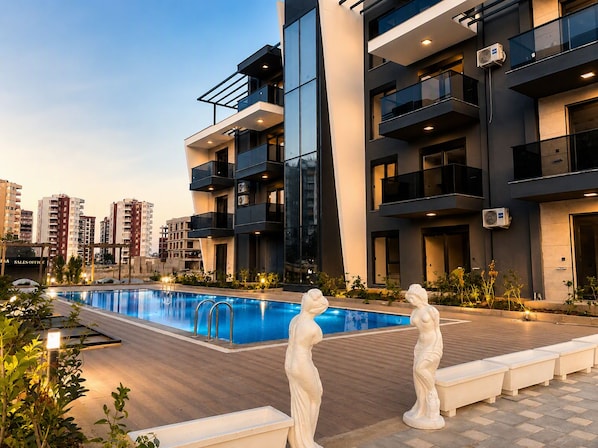 A modern apartment building with a swimming pool, outdoor lighting, and decorative statues. - Armin Luxury Suite (Antalya)
