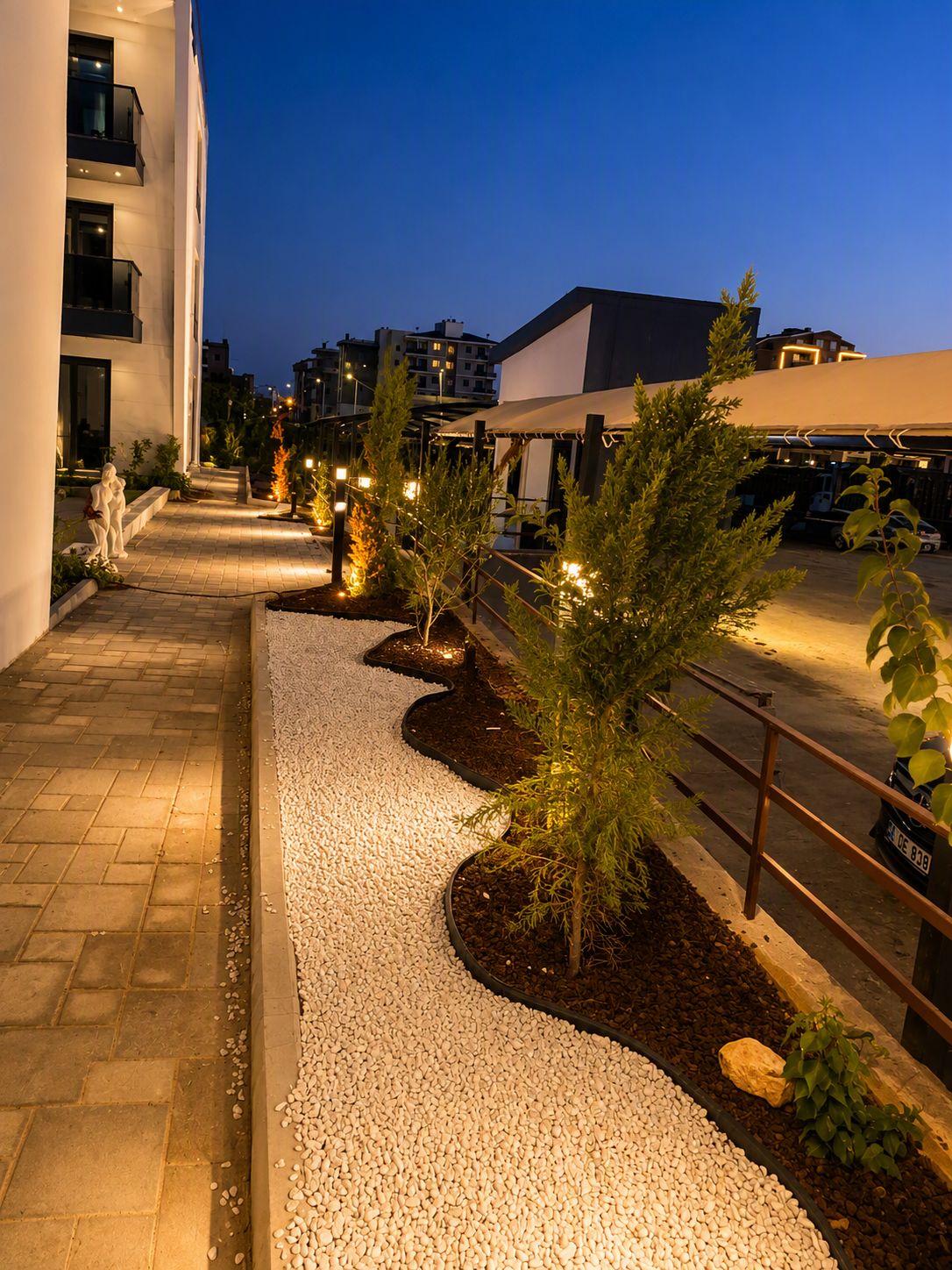 A nighttime outdoor pathway with gravel, small trees, and a statue.