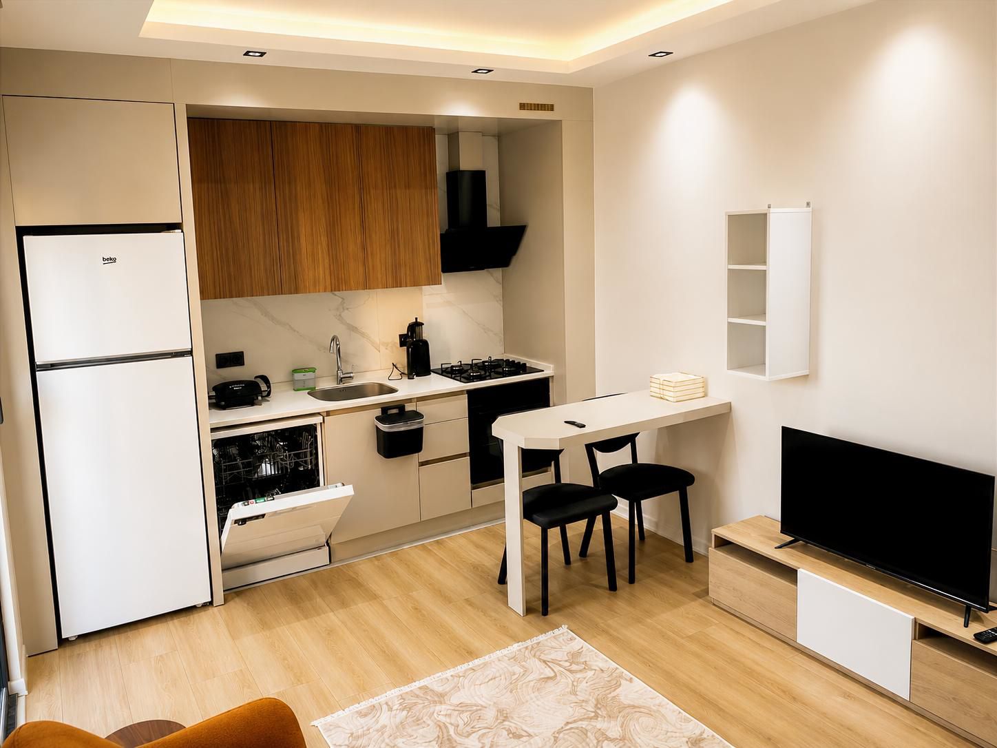 A compact kitchen with a refrigerator, stove, sink, and a dining area with chairs.