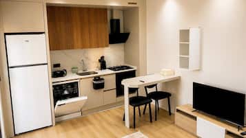 A compact kitchen with a refrigerator, stove, sink, and a dining area with chairs.