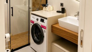 Ein kleines Badezimmer mit einer Duschkabine aus Glas, einer integrierten Waschmaschine und einem Waschbecken mit Spiegel.