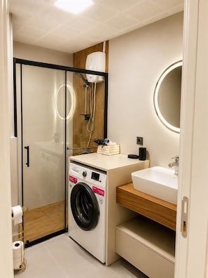 Casa de banho compacta com cabine de duche em vidro, máquina de lavar roupa integrada e lavatório com espelho.