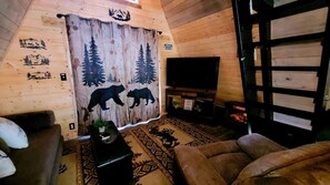 Een gezellig chaletinterieur met houten details, een open haard, een bank en een televisie.