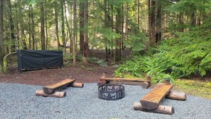 A campsite with a fire pit, a covered area, and a table set up on a gravel surface surrounded by trees. - A cozy A-Frame cabin for 2, just minutes from Mt. Rainier National Park (Ashford)