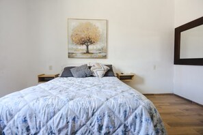 A bedroom with a bed, a nightstand, a wall-mounted painting, and a mirror.