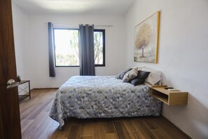 Een slaapkamer met een bed, een raam met gordijnen, een wandplank en een schilderij.