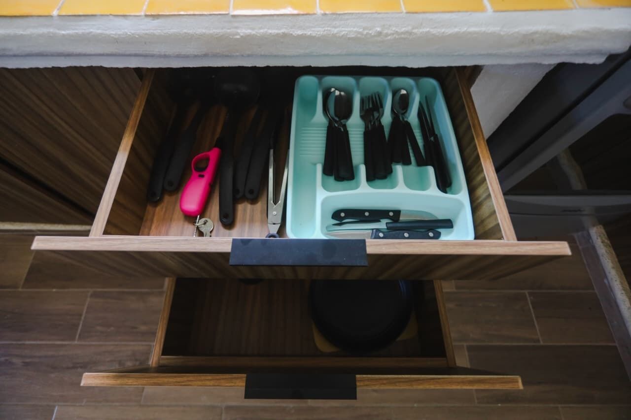 A drawer with kitchen utensils including knives, spoons, and a pink-handled knife.
