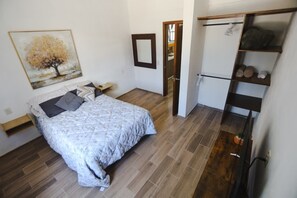 Een slaapkamer met een bed, een schilderij, een kledingkast en een plank met spullen.