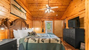 Une chambre dans une cabane en bois, comprenant un lit, une commode, un ventilateur de plafond et un téléviseur.