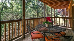 Une terrasse en bois avec une table ronde et des chaises, entourée d’une balustrade en bois, donnant sur une zone boisée.