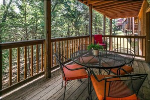 Eine Holzterrasse mit rundem Tisch und Stühlen, umgeben von einem Holzgeländer, mit Blick auf ein bewaldetes Gebiet.