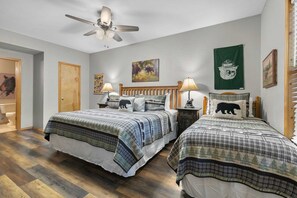 Een slaapkamer met twee bedden, een plafondventilator, houten vloeren en een groene wanddecoratie.