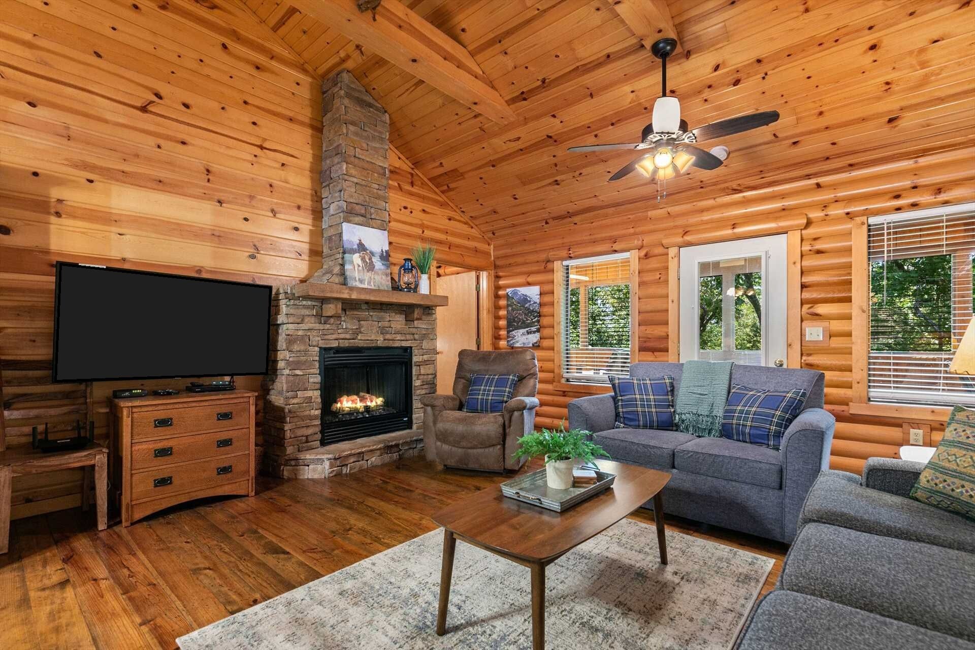 Ein Blockhaus-Interieur mit Kamin, Fernseher, einer Couch und Deckenventilator.
