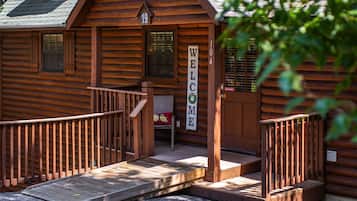 Une cabane en bois avec une pancarte « BIENVENUE », une véranda dotée d’une rampe d’accès et une pancarte « DÉFENSE DE FUMER ».