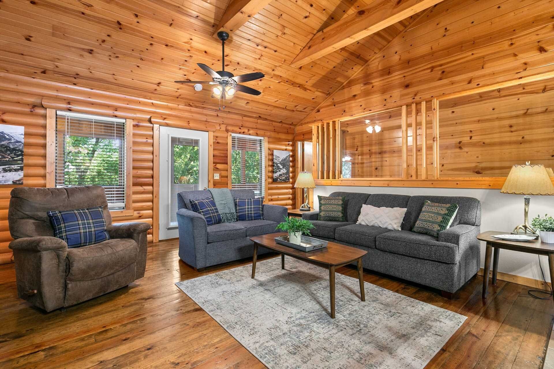 Ein rustikales Blockhaus-Interieur mit einer Couch, einem Sessel und einem Deckenventilator.