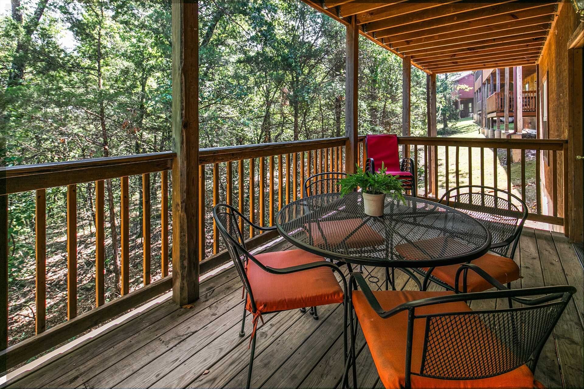 Une terrasse en bois avec une table ronde et des chaises, entourée d’une balustrade en bois, donnant sur une zone boisée.