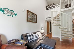 A living room with a leather sofa, a framed picture, a white staircase, and a wall-mounted air purifier. - Fantastic 3-bedroom condo in charming Gatlinburg near Ober Gatlinburg (Gatlinburg)